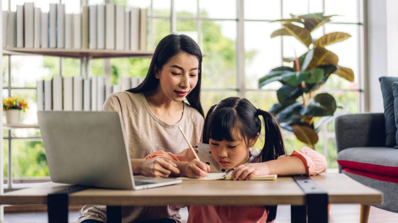 Mother and asian kid little girl learning and looking at laptop computer making homework studying knowledge with online education e-learning system.children video conference with teacher tutor at home